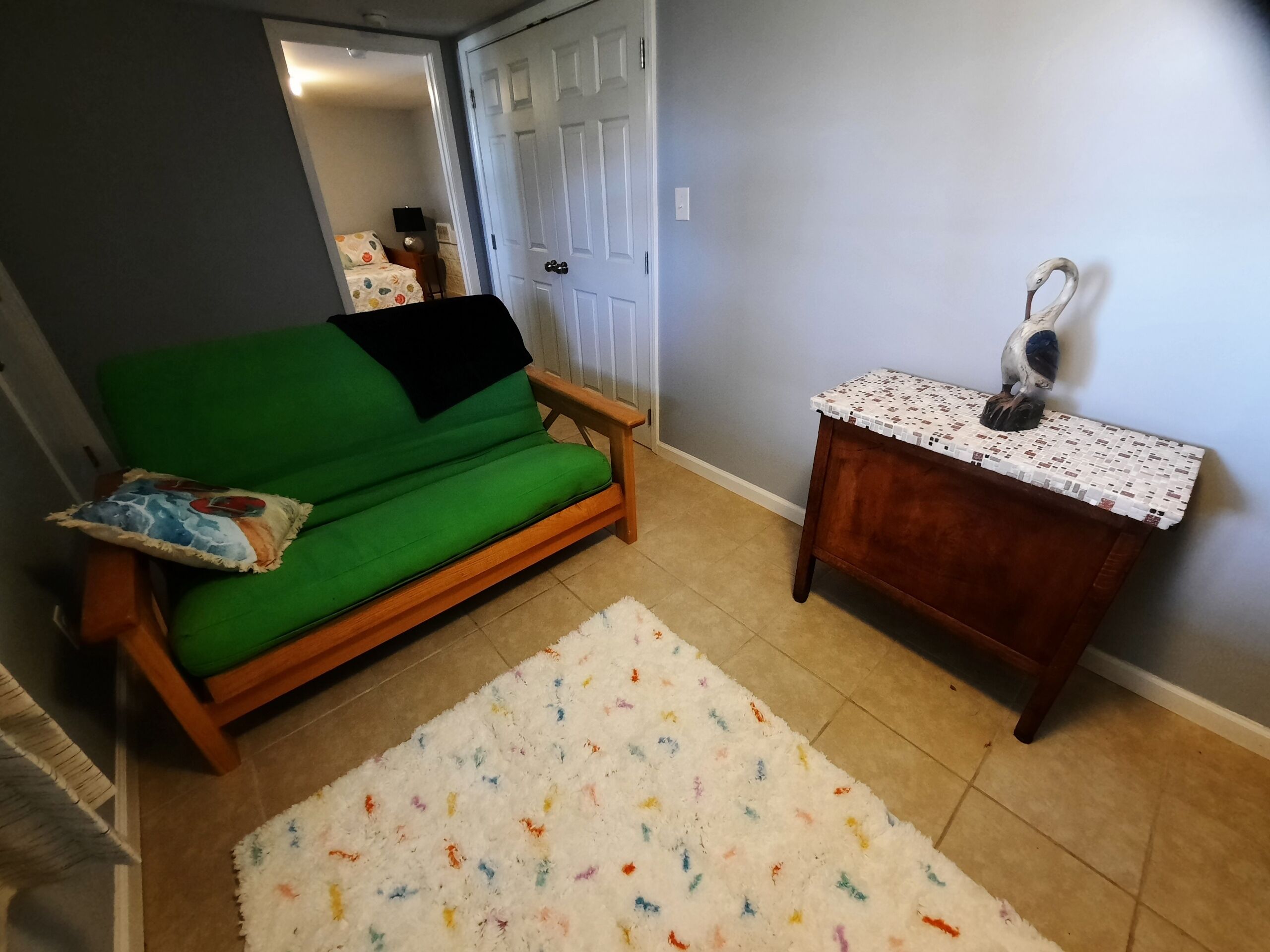 Ein kleiner Wohnbereich mit einem grünen Sofa, einem weißen Teppich mit bunten Mustern und einem Holznachttisch mit einem dekorativen Gegenstand.