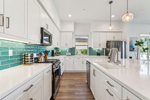 A modern kitchen with white cabinetry, a teal backsplash, and a central island.