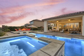 A swimming pool with a patio area, outdoor furniture, and a building with large windows.