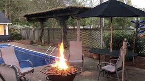 Un patio al aire libre con un hogar para fuego, sillones de descanso y una piscina.