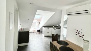 Moderni keittiö, jossa on kattovalokuvio, ruokailutila puupöydällä ja -tuoleilla sekä valkoinen keittiötaso.
