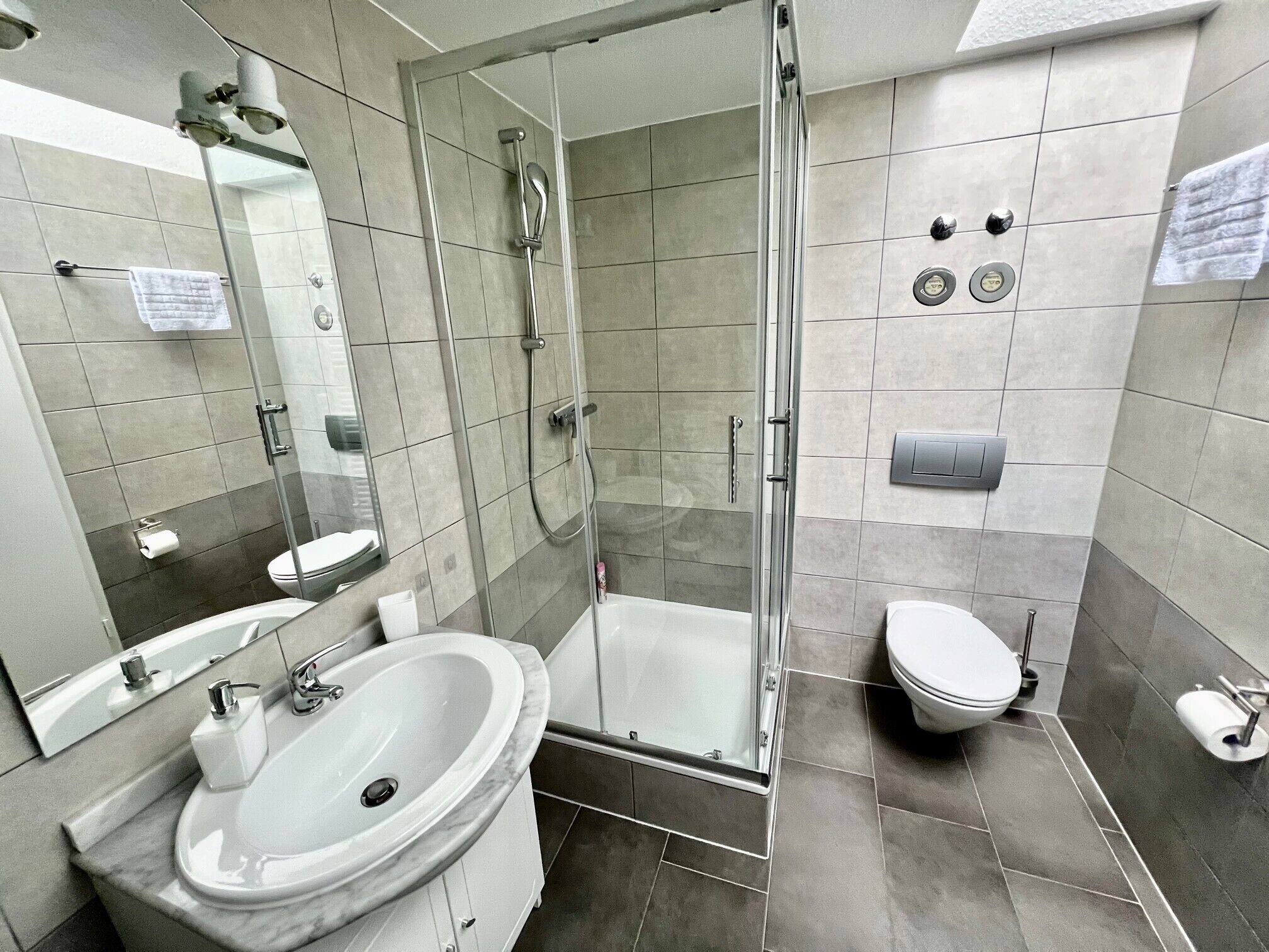 Ein modernes Badezimmer mit einer gläsernen Duschkabine, einem Waschbecken mit Marmorbecken und einer Toilette.