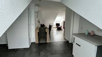 A spacious attic room with a sloped ceiling, a dining area with a table and chairs, and a kitchenette with cabinets and a countertop.