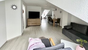 Moderni olohuone, jossa on taulutelevisio, sohva sekä ruokailutila, jossa on pöytä ja tuolit.