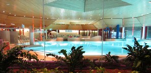 Une piscine intérieure moderne avec un plafond en bois, un espace détente et des sièges disposés autour de la piscine.