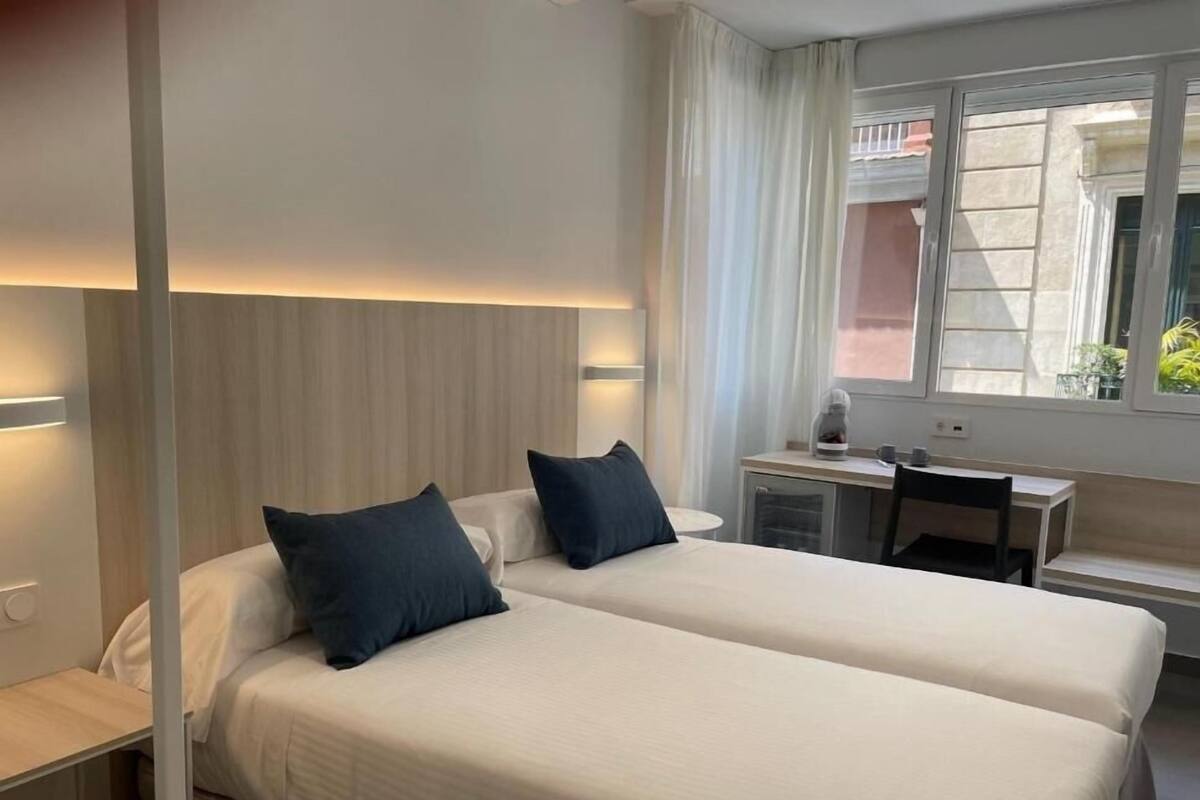 Ein Hotelzimmer mit zwei Betten, einem Schreibtisch und einem Fenster mit Vorhängen.