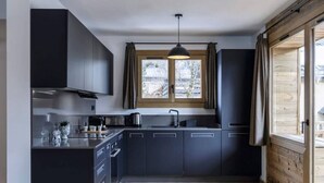 Una cocina moderna con armarios oscuros, una isla central, un ventanal con cortinas y suelo de madera.