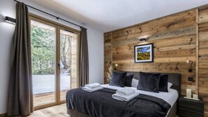 Un dormitorio moderno con una cama grande, paneles de madera en las paredes, un cuadro y vistas al exterior a través de una puerta corrediza.