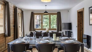 Un comedor con una mesa dispuesta para cuatro, un televisor en la pared y una ventana con cortinas.