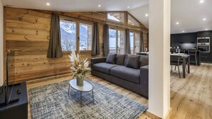 Una sala de estar moderna con un sofá gris, paredes de madera y un ventanal grande.