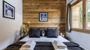 Un dormitorio con panel de pared de madera, una cama con ropa oscura, dos almohadas y un cuadro enmarcado sobre la cama.