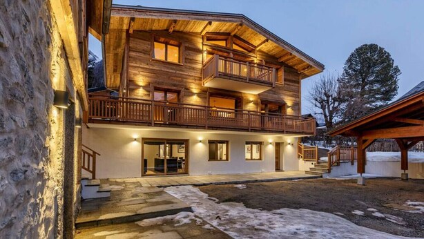 A multi-story wooden chalet with balconies, a stone facade, and a well-lit entrance.