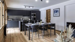 A modern kitchen with dark cabinets, a dining area with a table and chairs, and a wooden floor.