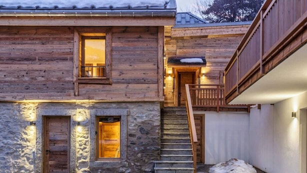 A wooden cabin with a stone entrance, a wooden staircase, and a balcony.