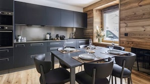 A modern kitchen with dark cabinetry, a dining area with a wooden table and chairs, and a large window with a view of the outside.
