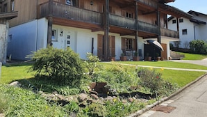 Una casa de madera de dos pisos con un balcón, un porche delantero y un jardín bien cuidado.