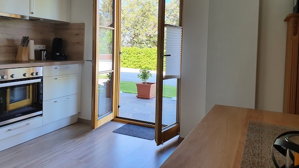 Una cocina moderna con armarios blancos, horno integrado y zona de comedor con mesa de madera.