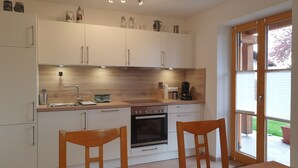 Una cocina moderna con armarios blancos, encimera de madera y una zona de comedor con dos sillas de madera.