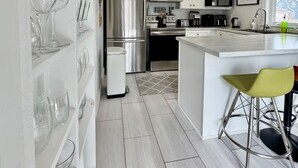 Una cocina moderna con armarios blancos, electrodomésticos de acero inoxidable y una barra con un taburete.