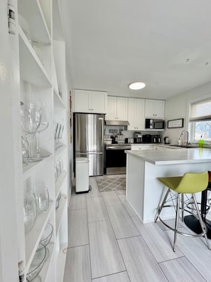 A modern kitchen with white cabinetry, stainless steel appliances, and a bar area with a stool. - Beautiful Brighton/Charlottetown; 1300 sq ft. apartment with AC and large deck.  (Charlottetown)