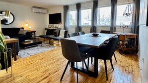 A modern living room with a dining area, wooden flooring, a ceiling fan, and large windows with curtains. - Beautiful Brighton/Charlottetown; 1300 sq ft. apartment with AC and large deck.  (Charlottetown)
