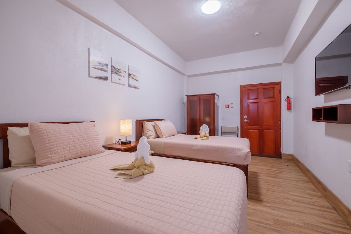 A hotel room with two beds, a wooden floor, a ceiling light, and a door.