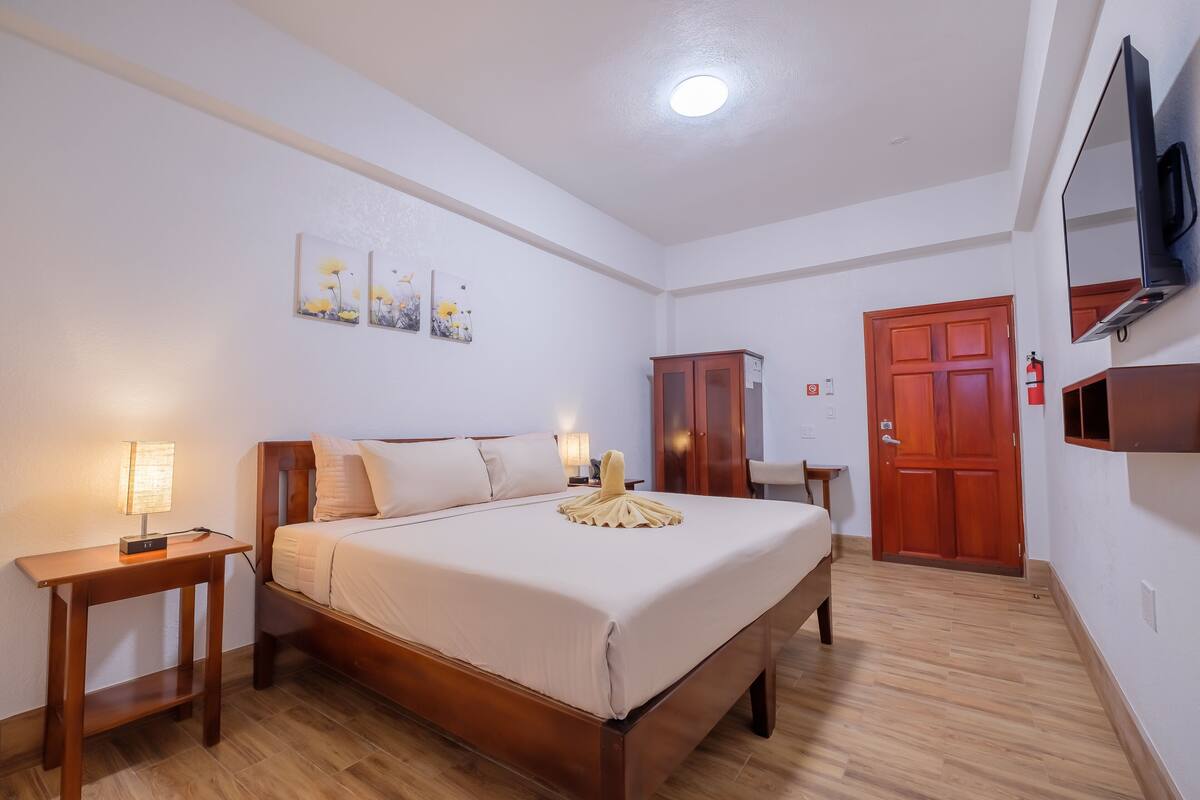 A hotel room with a bed, bedside tables, a wardrobe, a TV, and artwork on the wall.