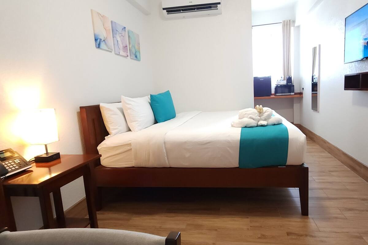 A neatly arranged hotel room with a bed, bedside table, lamp, and a television on the wall.