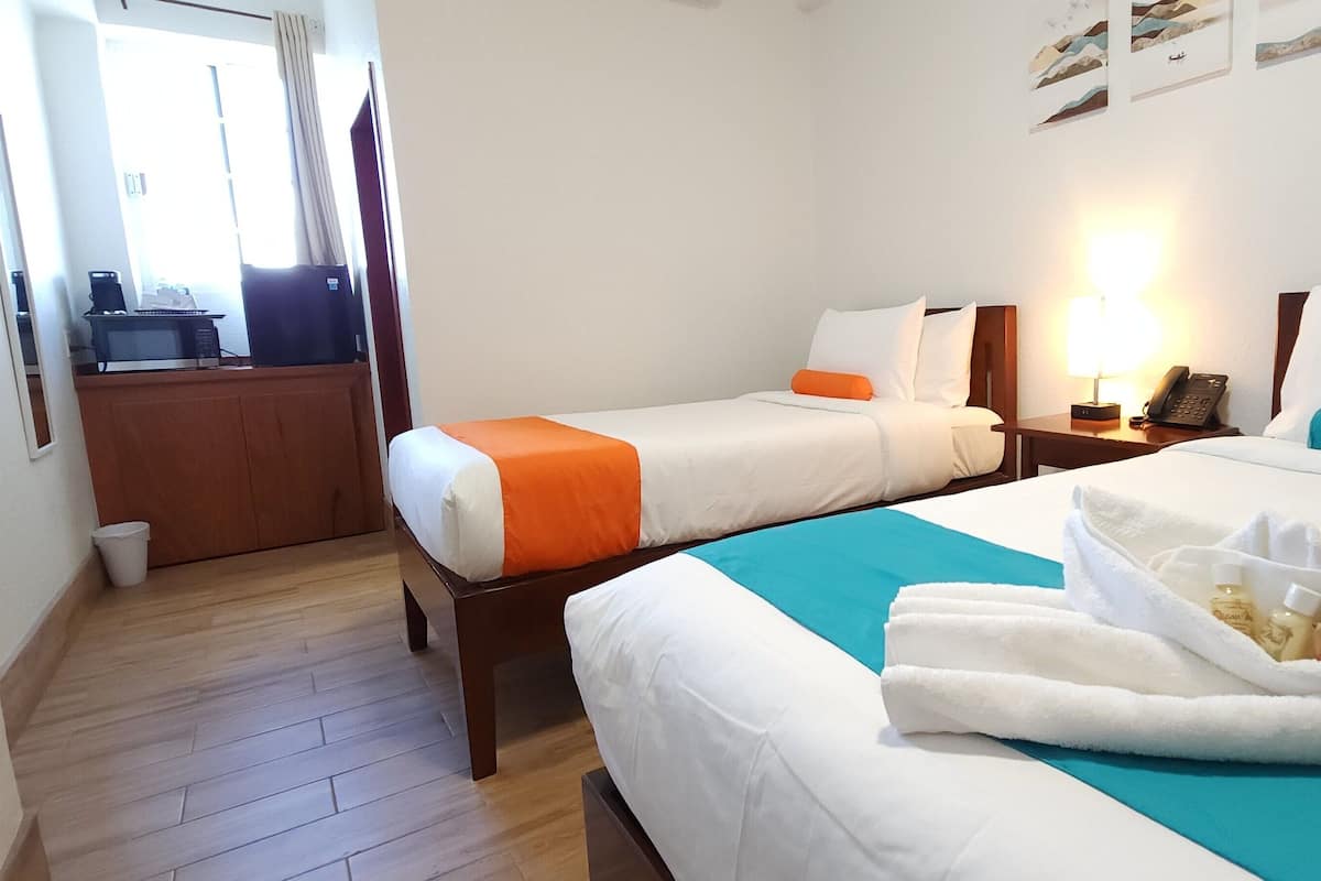 A hotel room with two beds, a wooden floor, a desk with a computer, and a window with curtains.