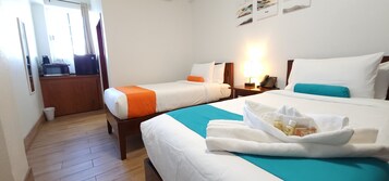 Een hotelkamer met twee bedden, een houten vloer, een bureau met een computer en een raam met gordijnen.