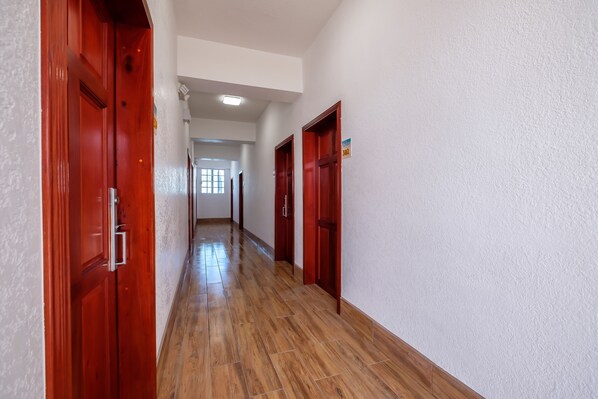 A hallway with wooden flooring and red doors, leading to a room with a window.