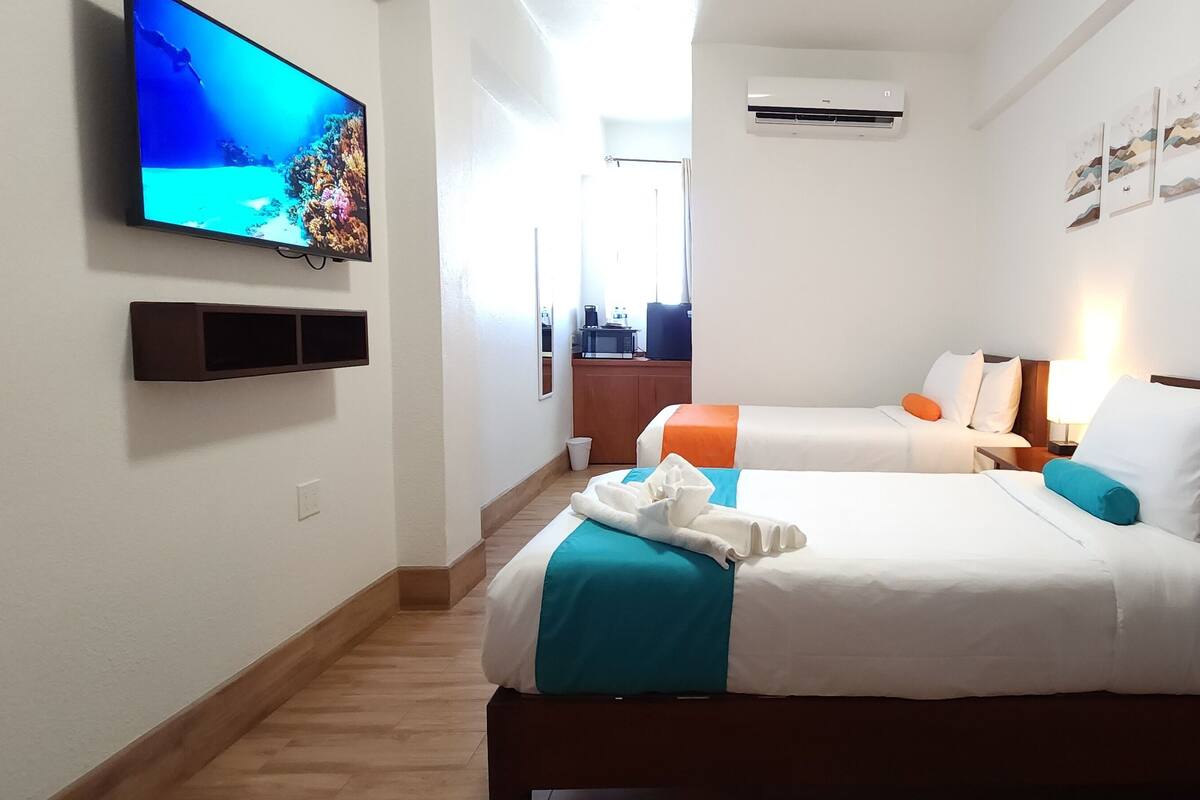 A hotel room with two beds, a TV on the wall, and a small kitchenette.
