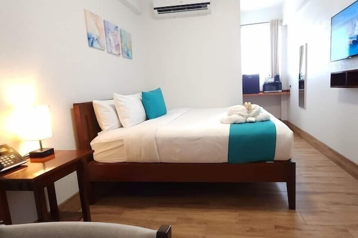 A hotel room with a bed, bedside table, lamp, and a television on the wall.