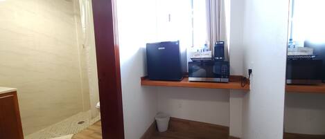 A bathroom with a shower, a toilet, a sink, and a shelf with a coffee maker and a box.