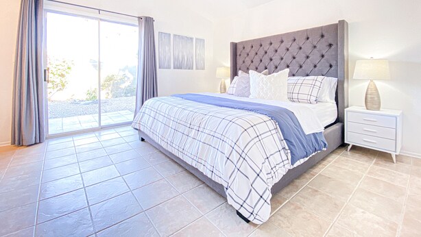 A bedroom with a large bed, a ceiling fan, a nightstand with a lamp, and a sliding glass door leading to an outdoor area. - LOCATION LOCATION LOCATION Gorgeous Villa Mystique (Palm Springs)