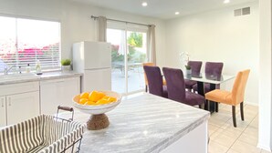 A modern kitchen with a marble countertop, a refrigerator, and a dining area with purple chairs. - LOCATION LOCATION LOCATION Gorgeous Villa Mystique (Palm Springs)