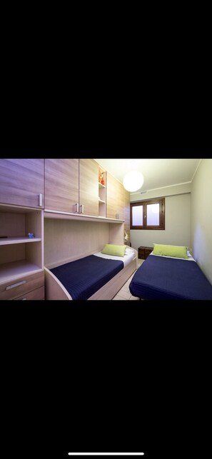 Ein Zimmer mit zwei Einzelbetten, Holzschränken, einem kleinen Tisch und einem Fenster.