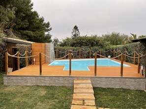 Eine Holzterrasse mit Schwimmbecken, umgeben von einem Seilabfangnetz und Steinstufen, die zu einer Holztür führen.