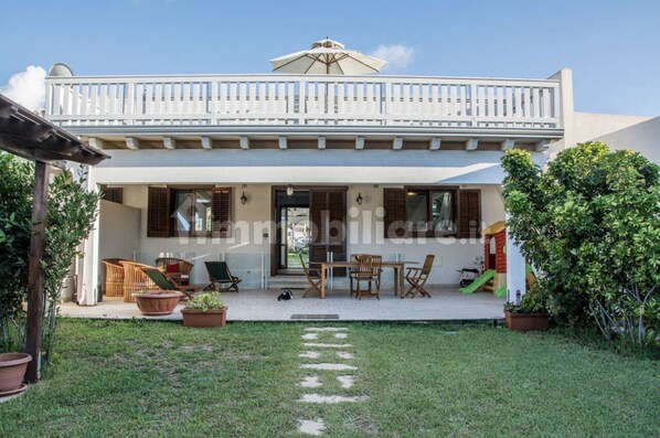 Ein zweigeschossiges Gebäude mit einem Balkon, einer Außenlounge und einem Gartenweg.