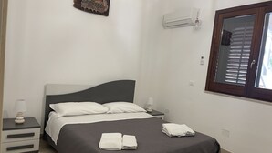 A bedroom with a bed, nightstands, a wall-mounted air conditioner, and a window with blinds. - Villa with pool and with sea view (San Vito Lo Capo)