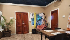A room with a wooden floor, a dining table with chairs, a hanging chair with cushions, and two wooden doors.