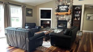 Una sala de estar con chimenea de piedra, sofás de cuero, un televisor de pantalla plana y una estantería.