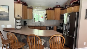 Una cocina con armarios de madera, un refrigerador de acero inoxidable y una isla de piedra con taburetes de bar.