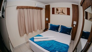 Una habitación de hotel con una cama grande, una mesita de noche, un espejo y una ventana con cortinas.