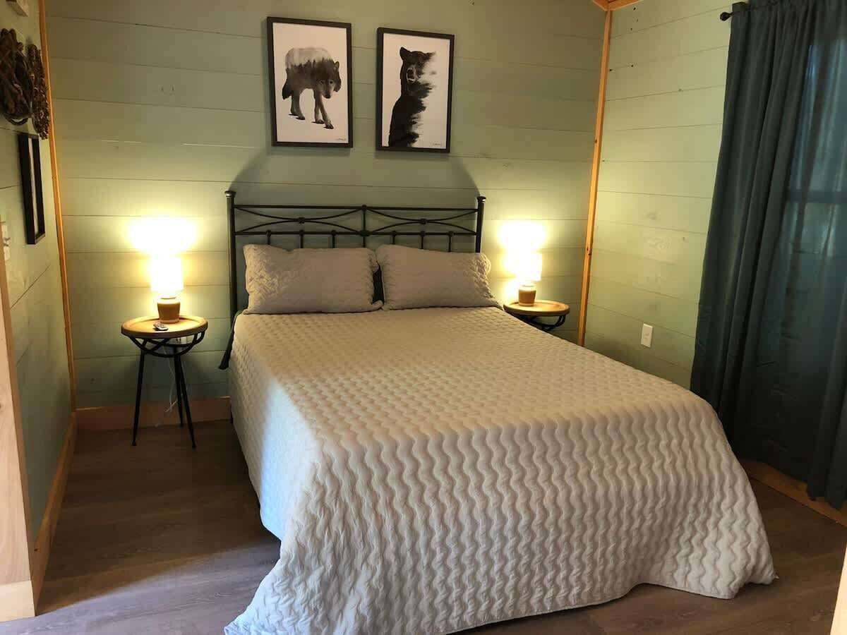 A bedroom with a bed, two bedside lamps, a headboard, and two framed pictures on the wall.