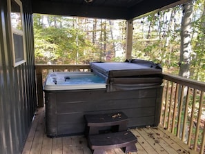 Een hottub op een houten terras met uitzicht op een bos.