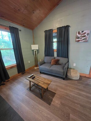 A room with a sofa, a wooden coffee table, a lamp, and a window with curtains.