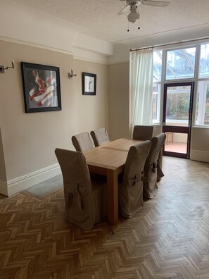 A dining area with a wooden table and chairs, a ceiling fan, and a large window with curtains.