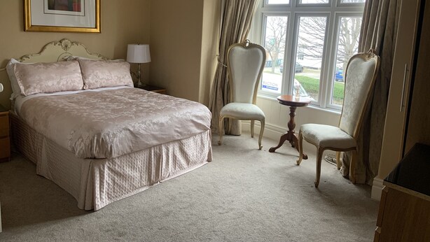A bedroom with a large bed, two chairs, a small table, and a window with curtains.