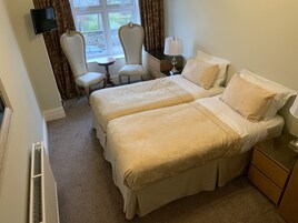 Habitación de hotel con dos camas, una mesita, una silla, televisión y ventana con cortinas.